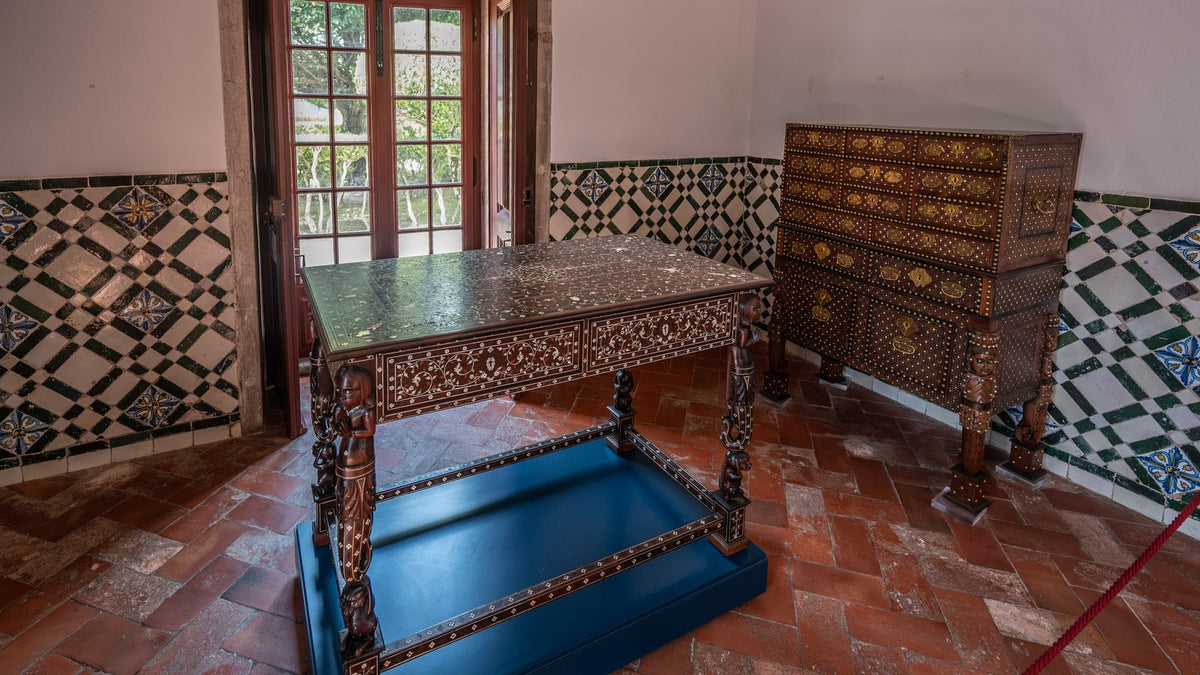 Dark antique wood furniture in a tiled room with terracotta herringbone flooring and blue geometric wall tile.