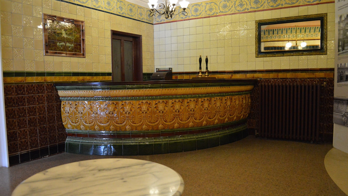 Historic tiled pub interior with moulded ceramic borders wrapping walls and architectural openings.