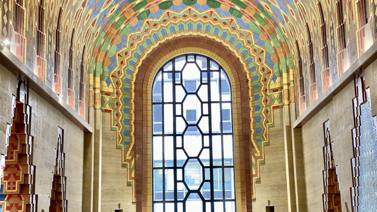 Art Deco lobby in Detroit with a polychromatic tile ceiling, geometric mosaic, stone walls, and metal details.
