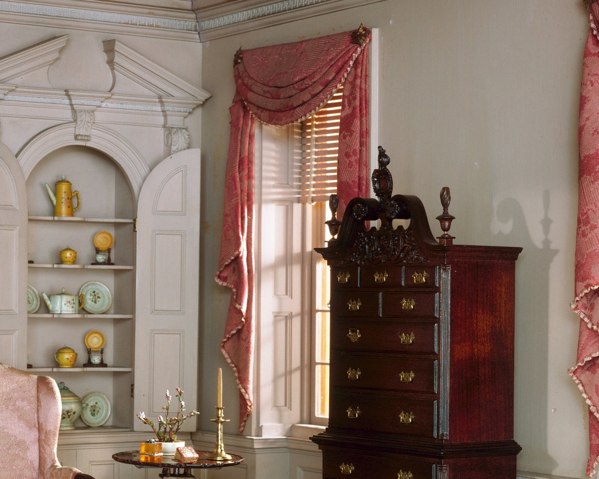 A miniature Pennsylvania drawing room with a tall chest, fireplace, drapery, and small decorative objects arranged at several scales.