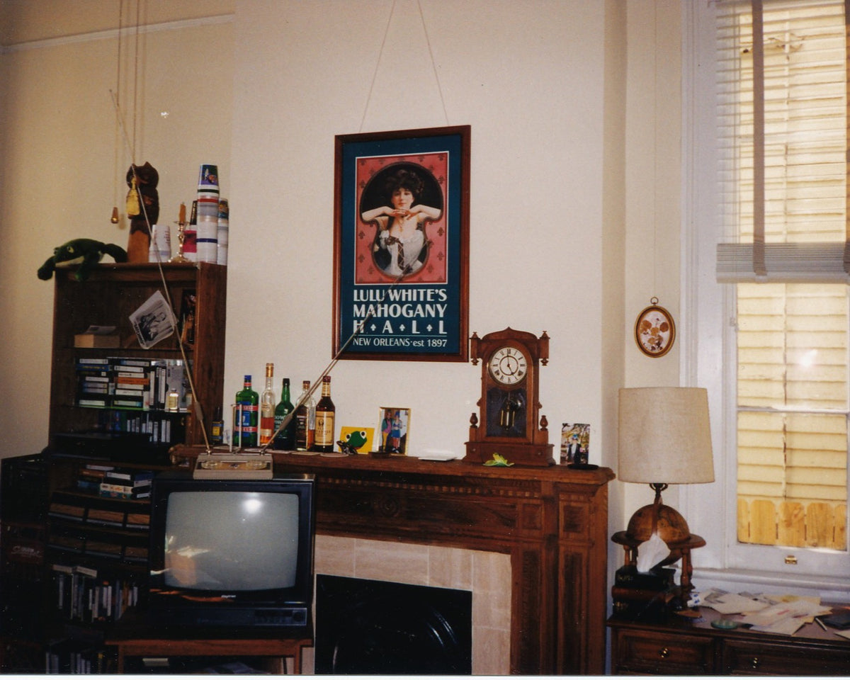 A New Orleans living room photographed in 1998 with a wood mantel, CRT television, shelves, lamps, family photographs, and collected objects.