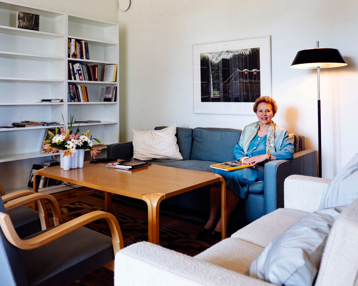 A 1994 Finnish living room with pale walls, a blue sofa, light wood furniture, a geometric rug, and one large framed artwork.