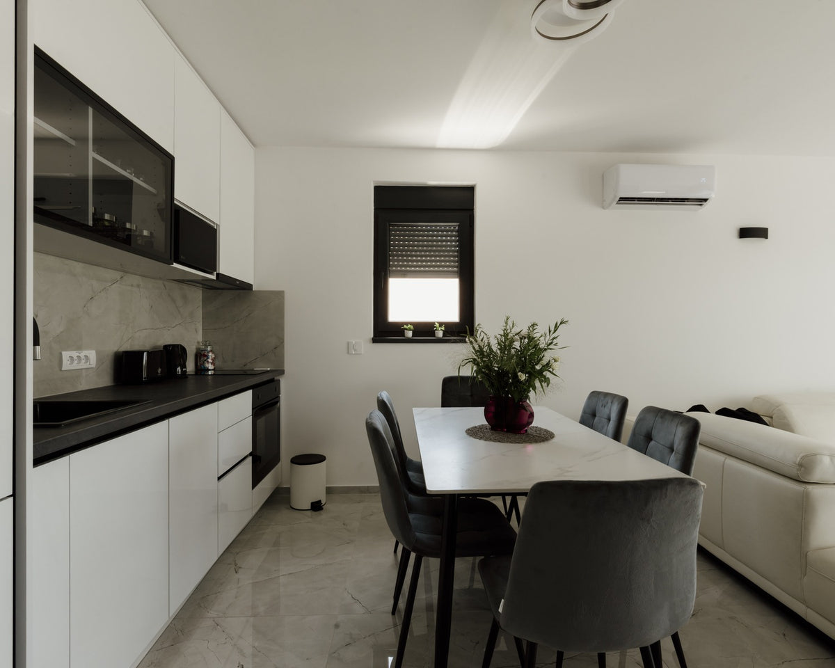 White kitchen and dining area with pale cabinetry, grey floor tile, and minimal decoration.
