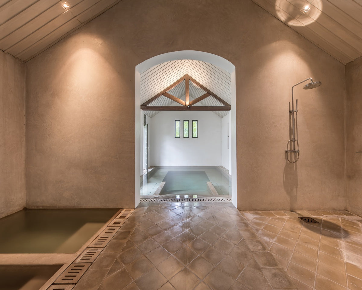 Indoor spa pool with warm plaster walls, pale tile, dark timber, and a recessed shower.