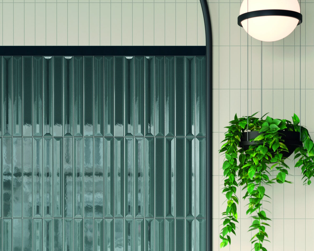Glossy deep-teal relief tile beside a pale matte tile wall, lit by a round wall lamp.