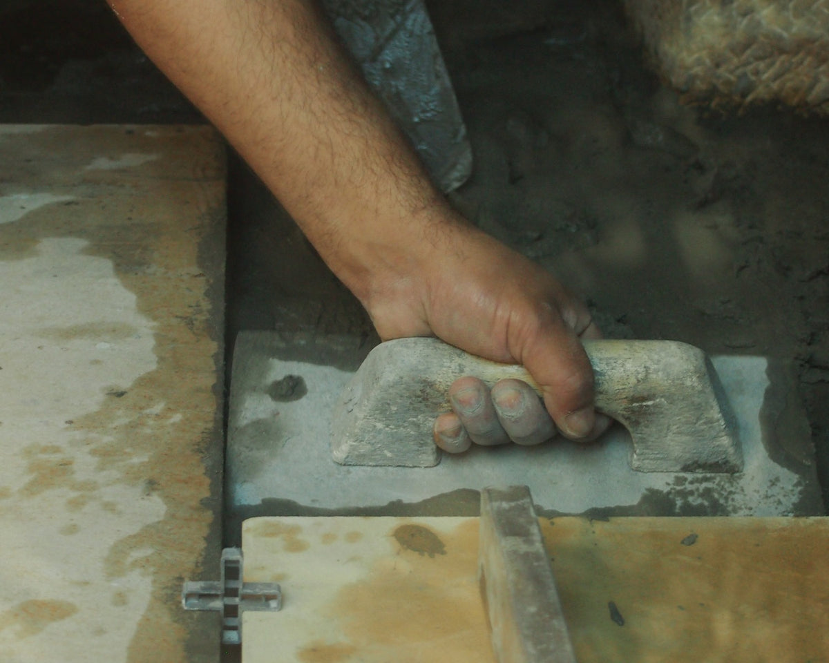 Installer using a trowel beside aligned floor tiles and plastic spacers.