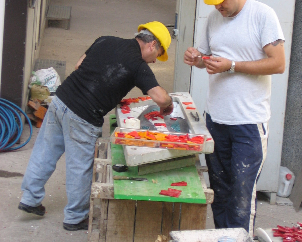 Two mosaic artisans assembling colored pieces by hand on a worktable at the Sagrada Familia.