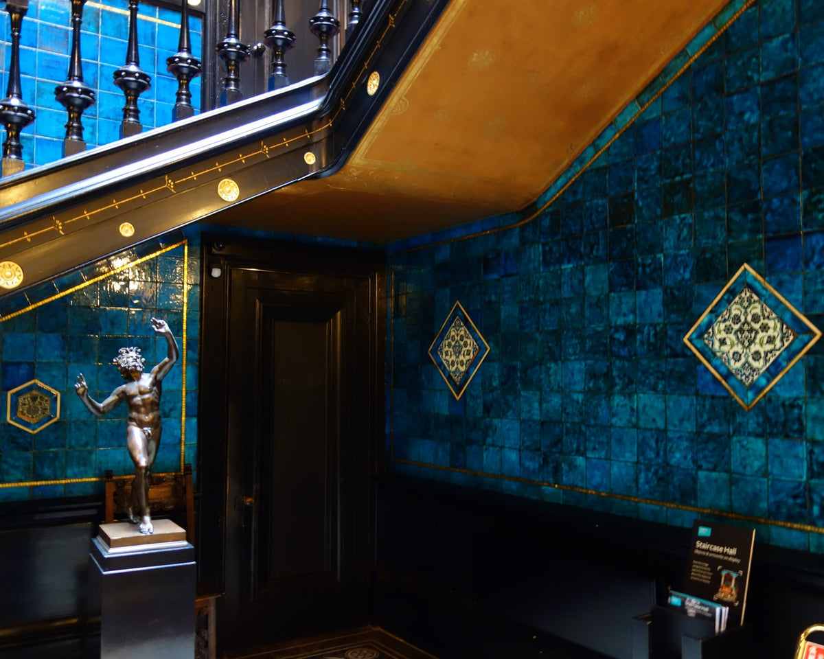 Blue-green William De Morgan tiles wrap the staircase hall at Leighton House Museum.