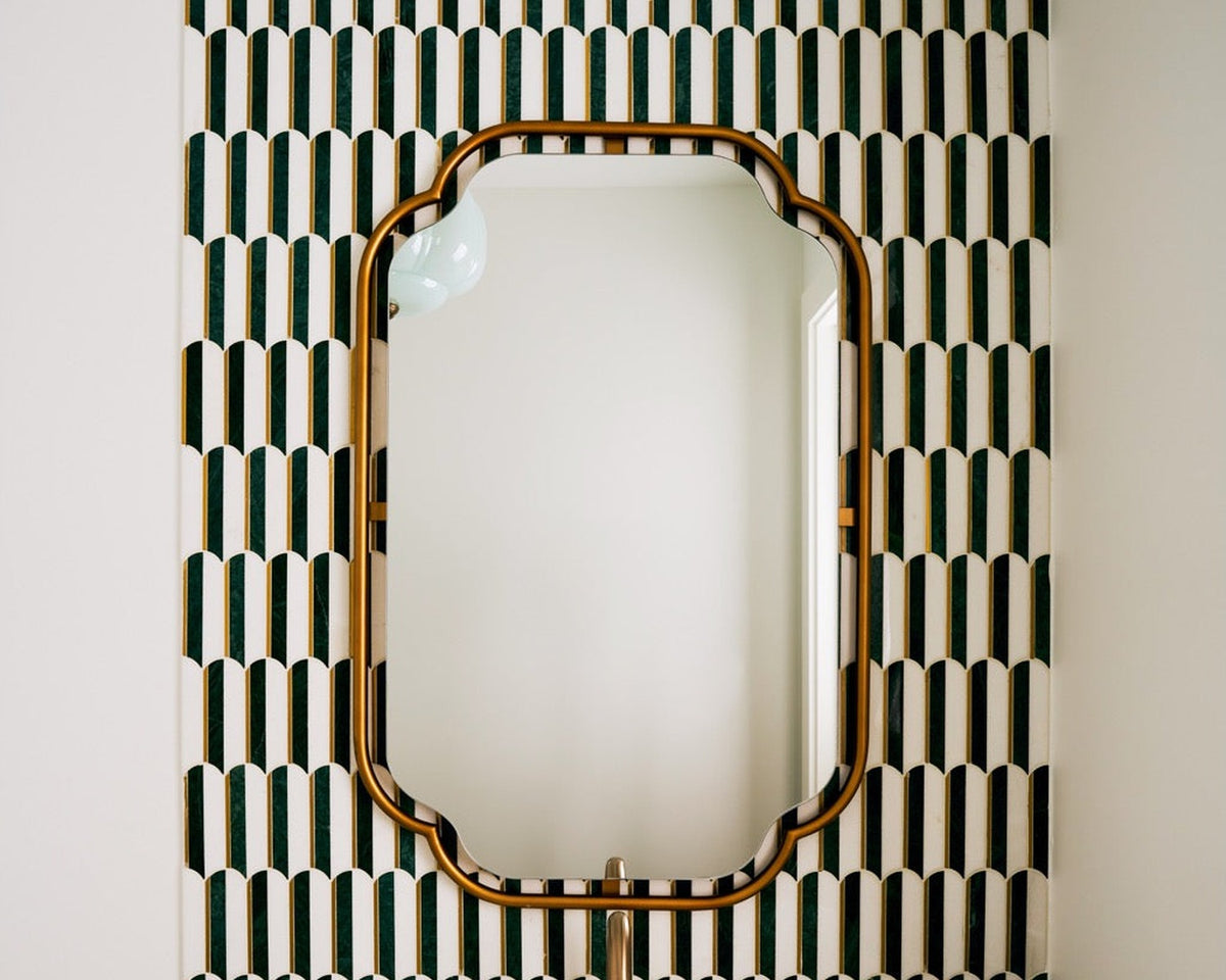 Cadenza green and white mosaic surrounding a brass-edged bathroom mirror.