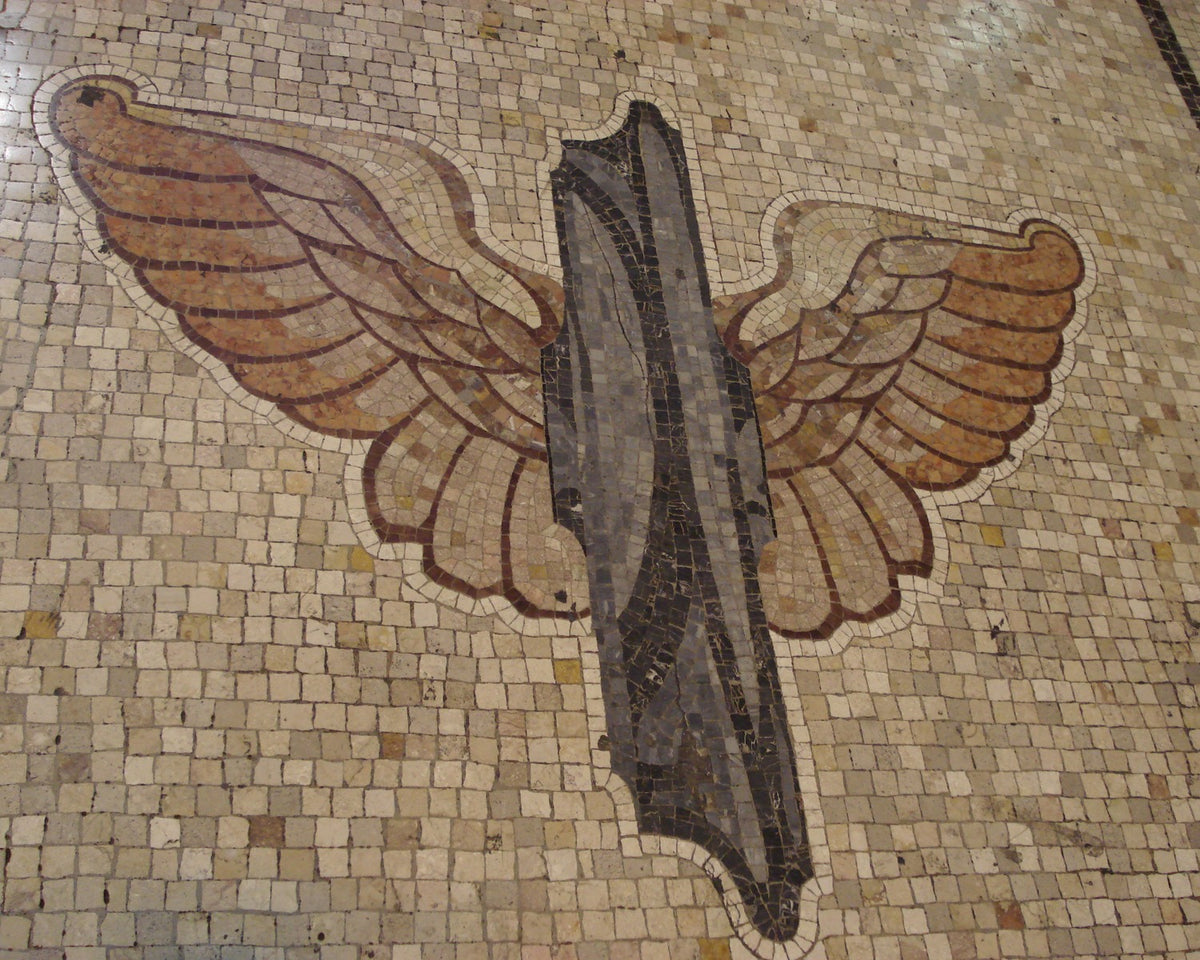 Symmetrical winged-wheel mosaic in cream, amber and black on the floor of Milano Centrale.