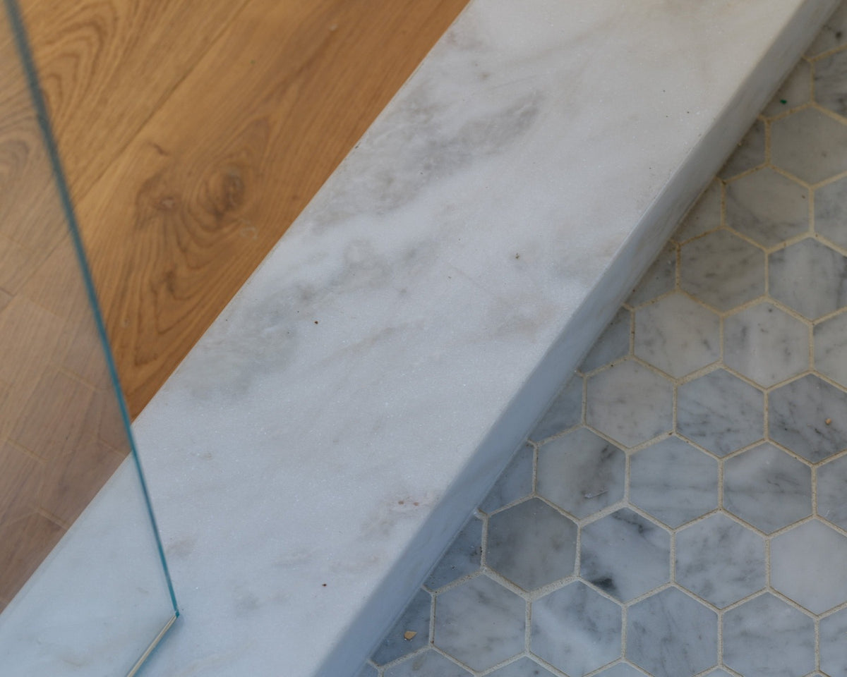Cygne Blanc mosaic meeting a marble threshold, wood floor, glass panel, and grout joints.