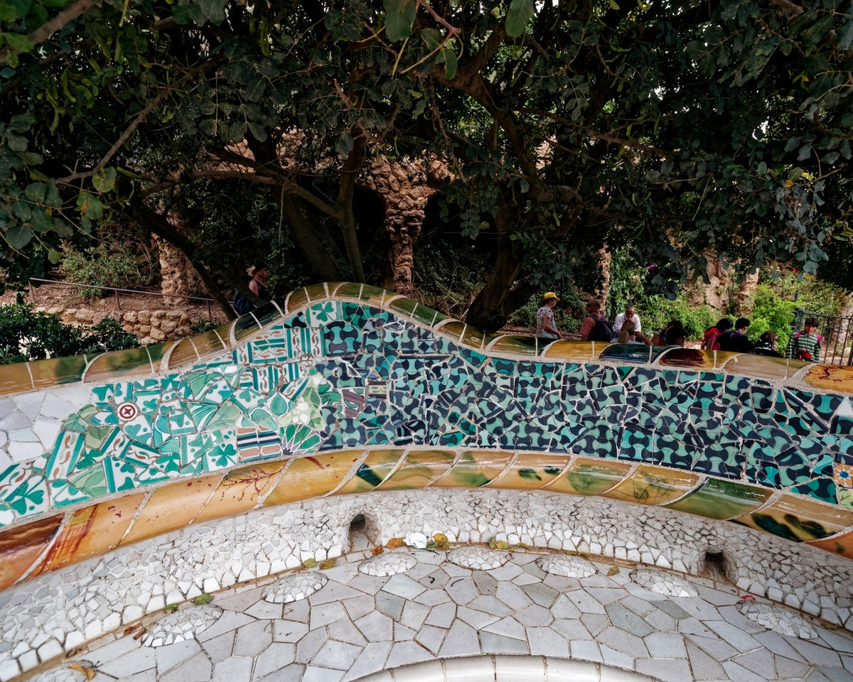 Curved mosaic benches at Park Guell covered in many small colored ceramic fragments.