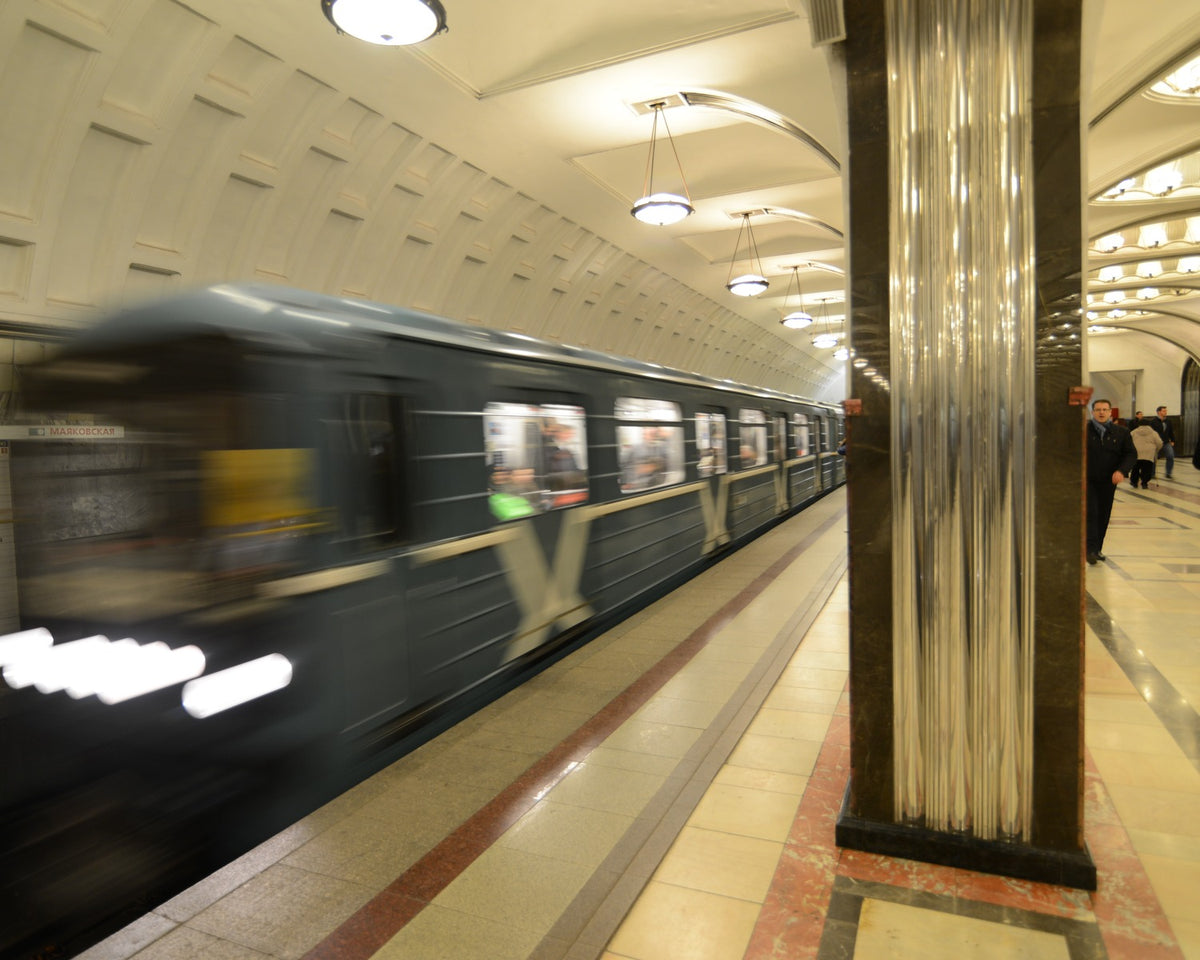 Art Deco metro station with repeated arches, stainless-steel columns, marble surfaces, and illuminated ceiling mosaics.