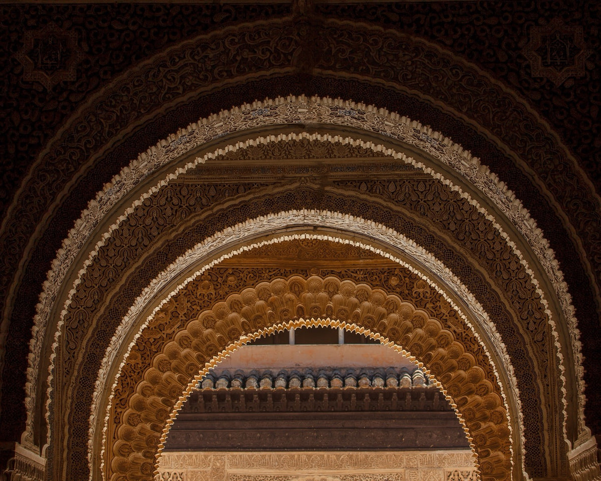 Nested ornamented arches at the Alhambra, where repeated curves, borders, carving, and contrast create a hierarchy from room scale to hand scale.