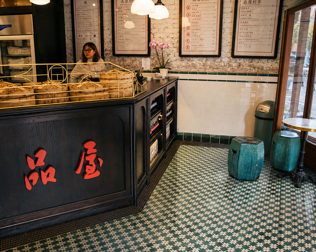 A restaurant interior where a green and white patterned tile floor organizes the counter, stools, circulation path, and surrounding material palette.